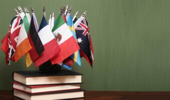 World flags on a pile of books in front of a green chalkboard